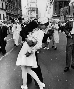 A jubilant Amer. sailor clutching a white-uniformed nurse in a back-bending, passionate kiss as he vents his joy while thousands jam the Times Square area to celebrate the long awaited victory over Japan.